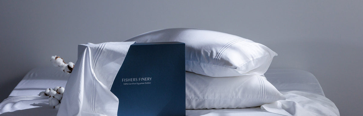 Fishers Finery Certified Egyptian Cotton Sheet Set on a bed with two pillows and gift box and piece of cotton behind the pillows