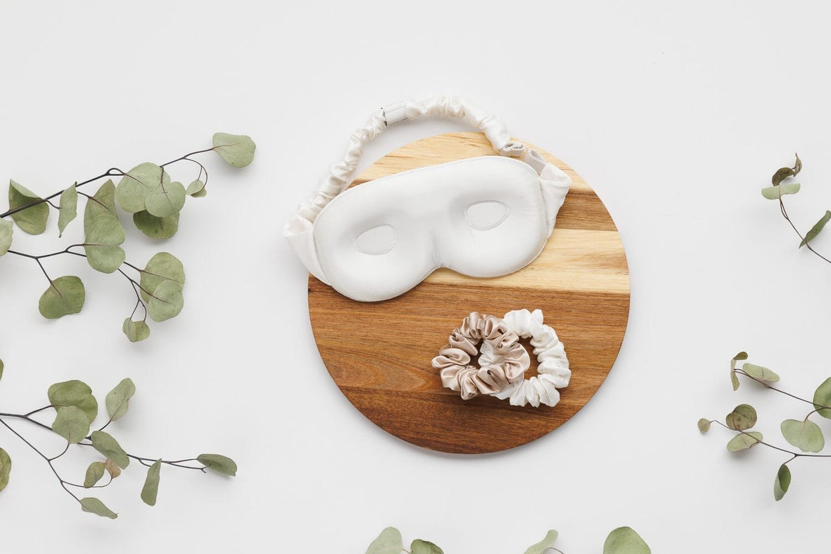 Silk sleep mask and silk scrunchies on a round wood board with eucalyptus