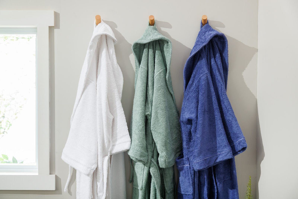 White, sage and blue hooded terry robes hanging on wooden wall pegs