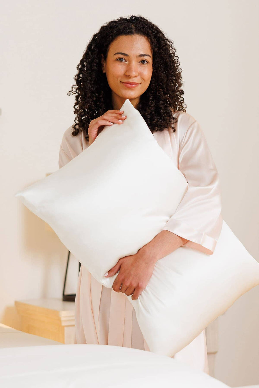 Woman holding two pillows in natural white silk pillowcases.