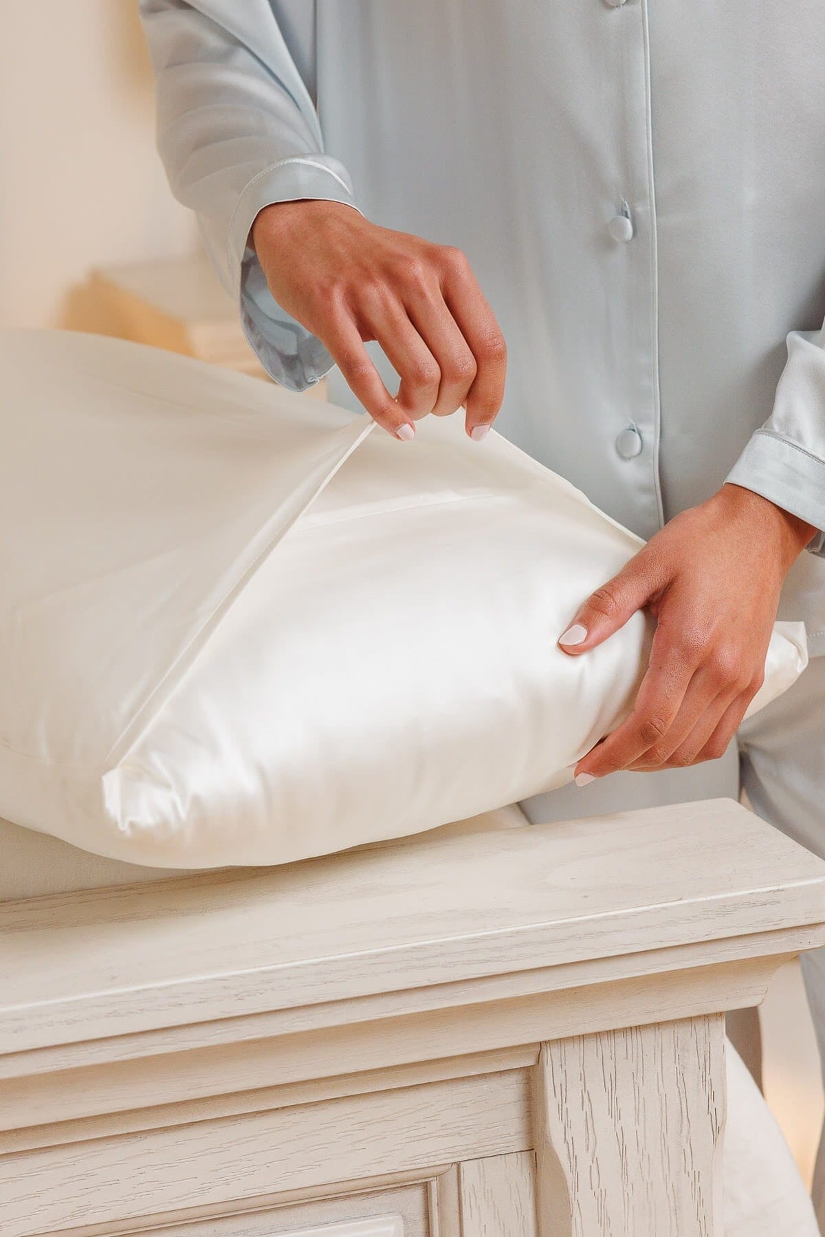 Natural white silk pillowcase with smooth, lustrous texture being adjusted on pillow.