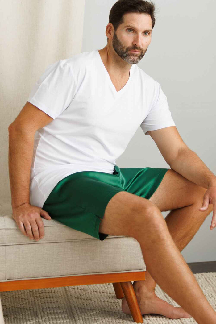 White silk short-sleeve V-neck shirt paired with green shorts, worn by seated male model.