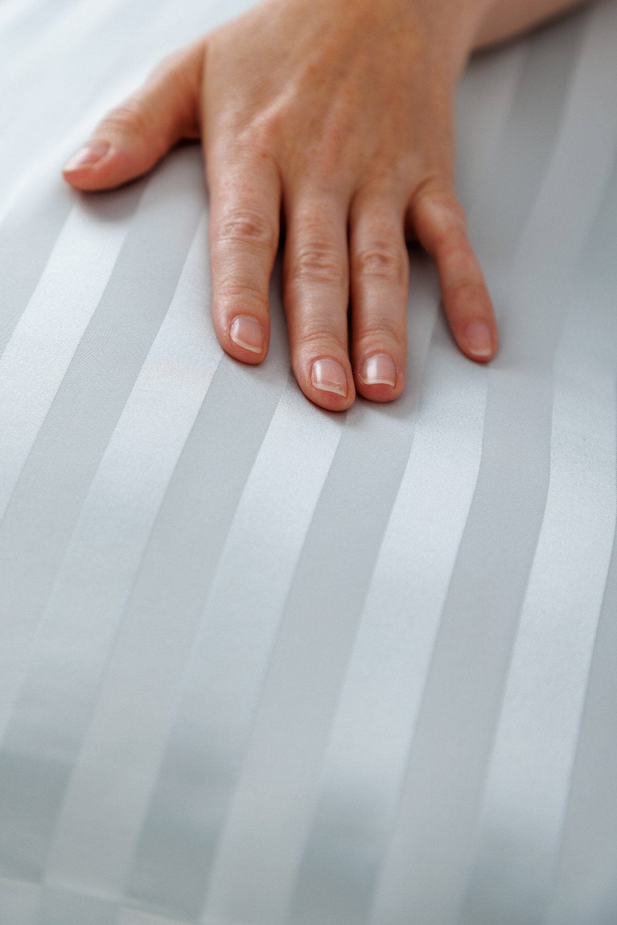 Silver silk pillowcase with subtle striped pattern and smooth texture.