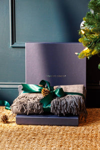gray cashmere throw folded and wrapped in a green bow on top a blue gift box