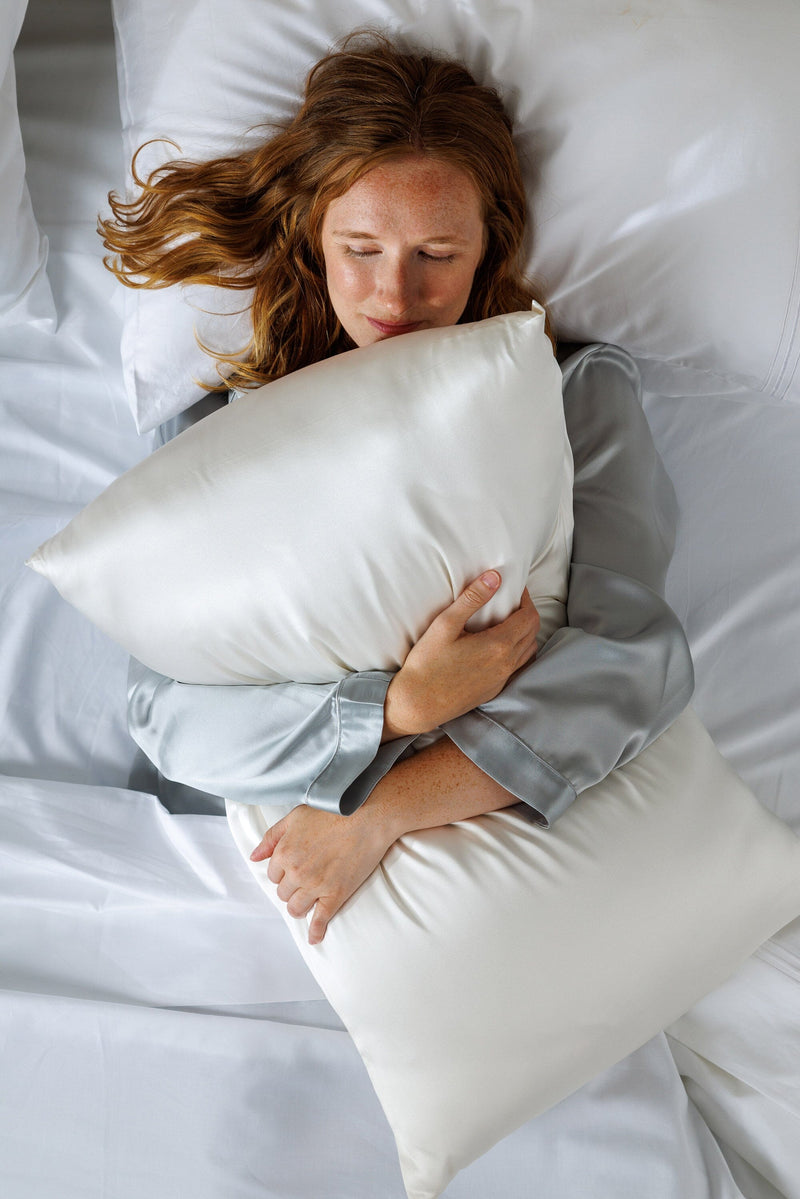 Natural white silk pillowcase with smooth, shiny texture on a bed.