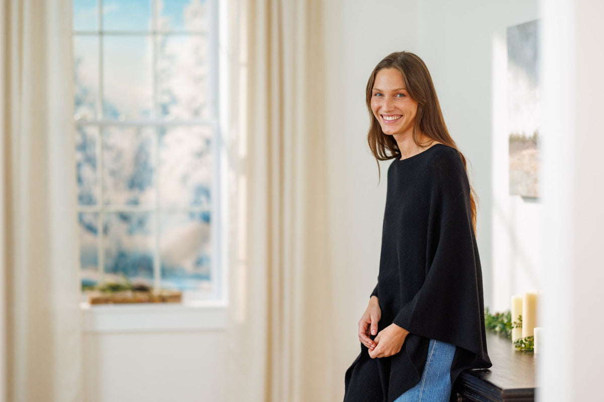 Woman in a black cashmere poncho smiling by a sunlit window