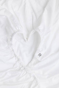 A close-up of a white fitted sheet with an elasticized band, featuring a heart-shape and a small tag that says "Long Side".
