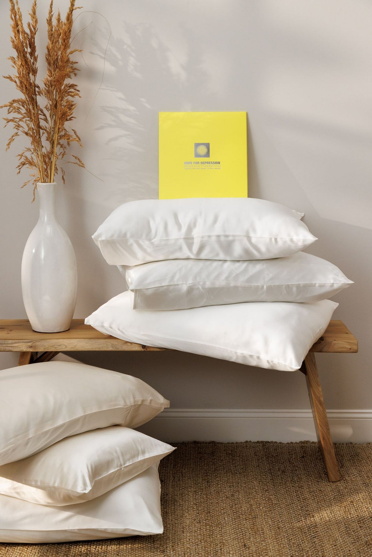 Natural white organic silk pillowcases stacked on a wooden bench and on the floor, with the yellow Hope for Depression Research Foundation gift box