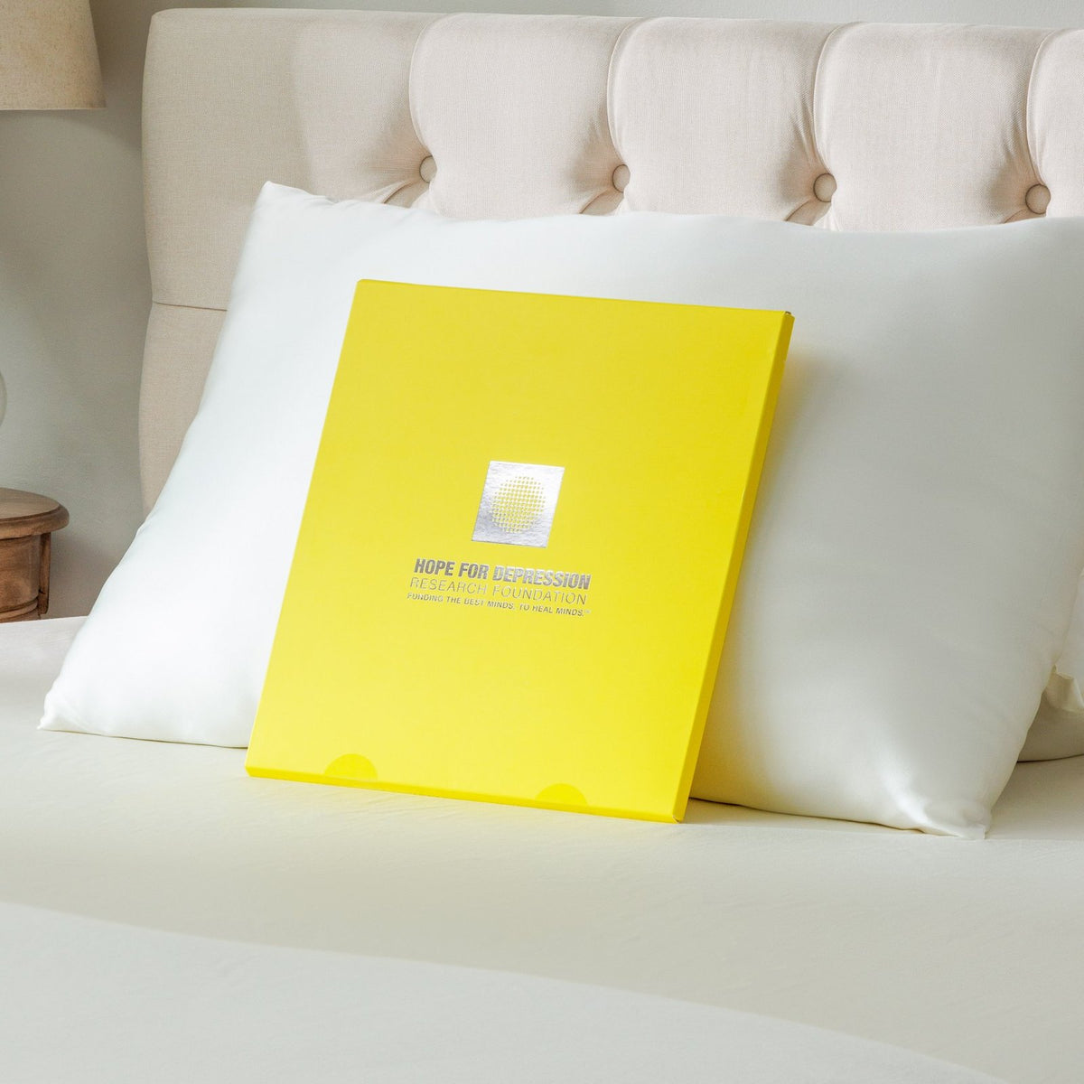 Natural white organic silk pillowcase on a bed with the yellow Hope for Depression Research Foundation gift box