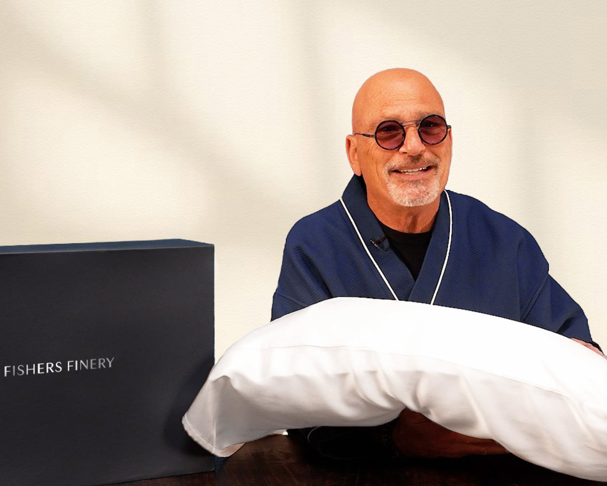Howie Mandel holding a pillow with a silk pillowcase wearing a robe.