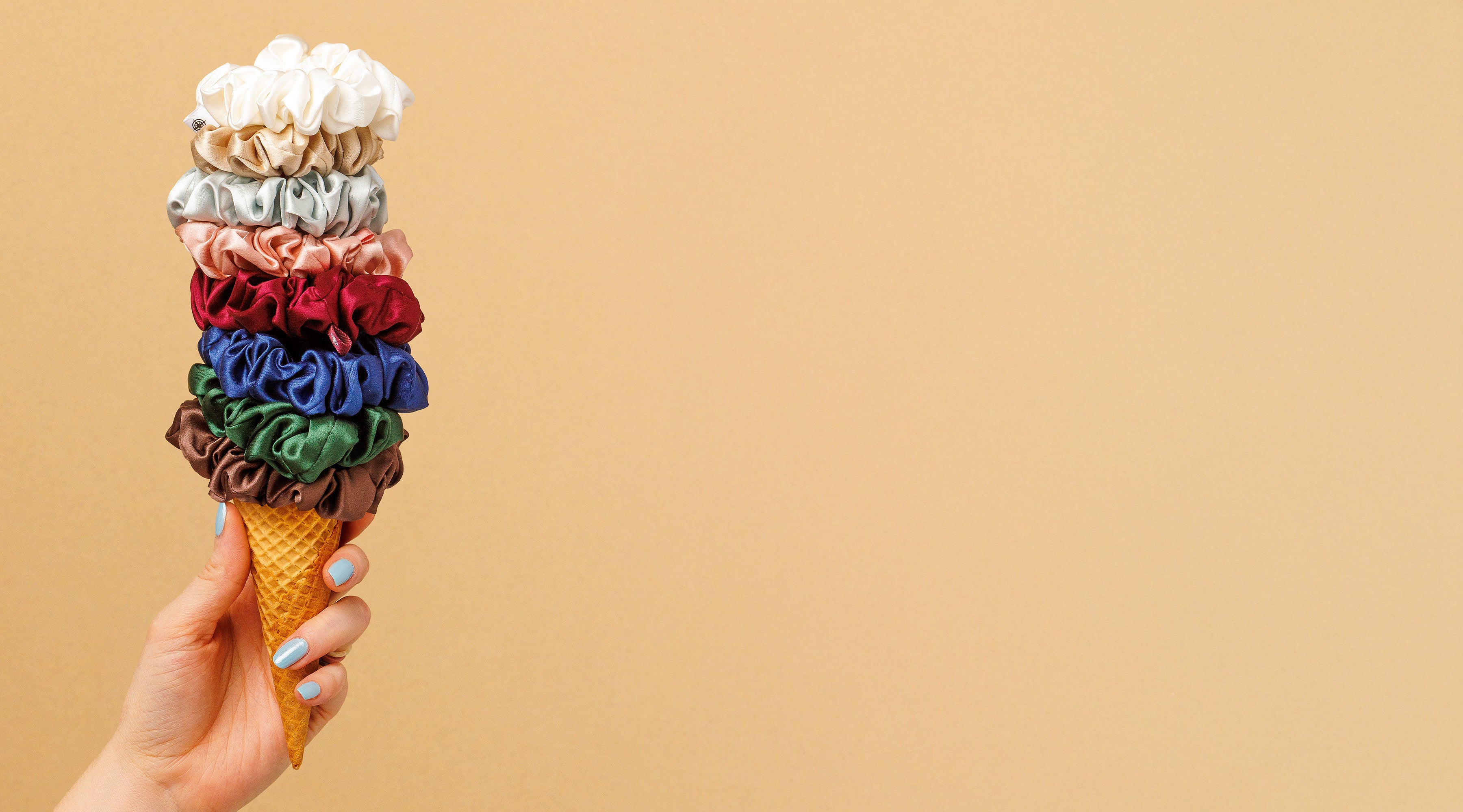 Hand holding a colorful ice cream cone-made with scrunchies against a beige background
