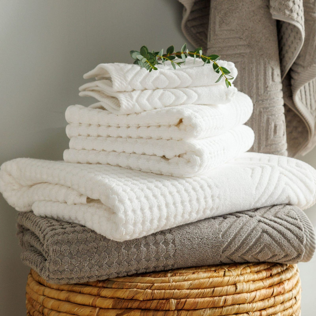Diamond jacquard organic cotton bath towels, hand towels and washcloths stacked on a woven stool