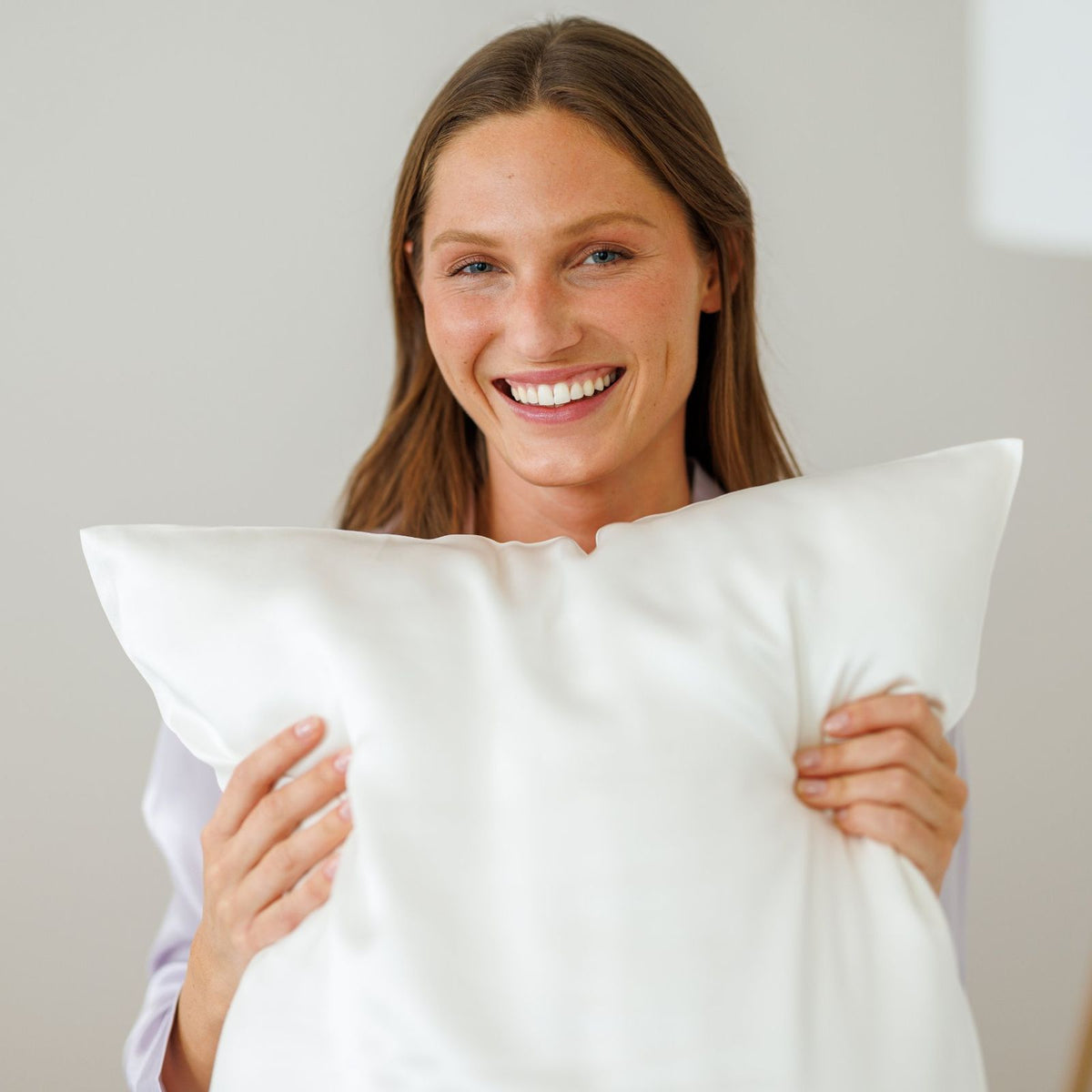 Smiling woman hugging a pillow in a white mulberry silk pillowcase