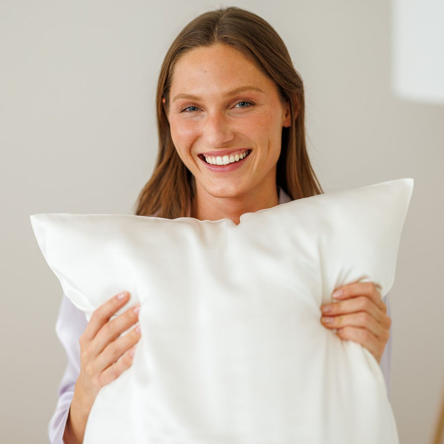 Smiling woman hugging a pillow in a white silk pillowcase