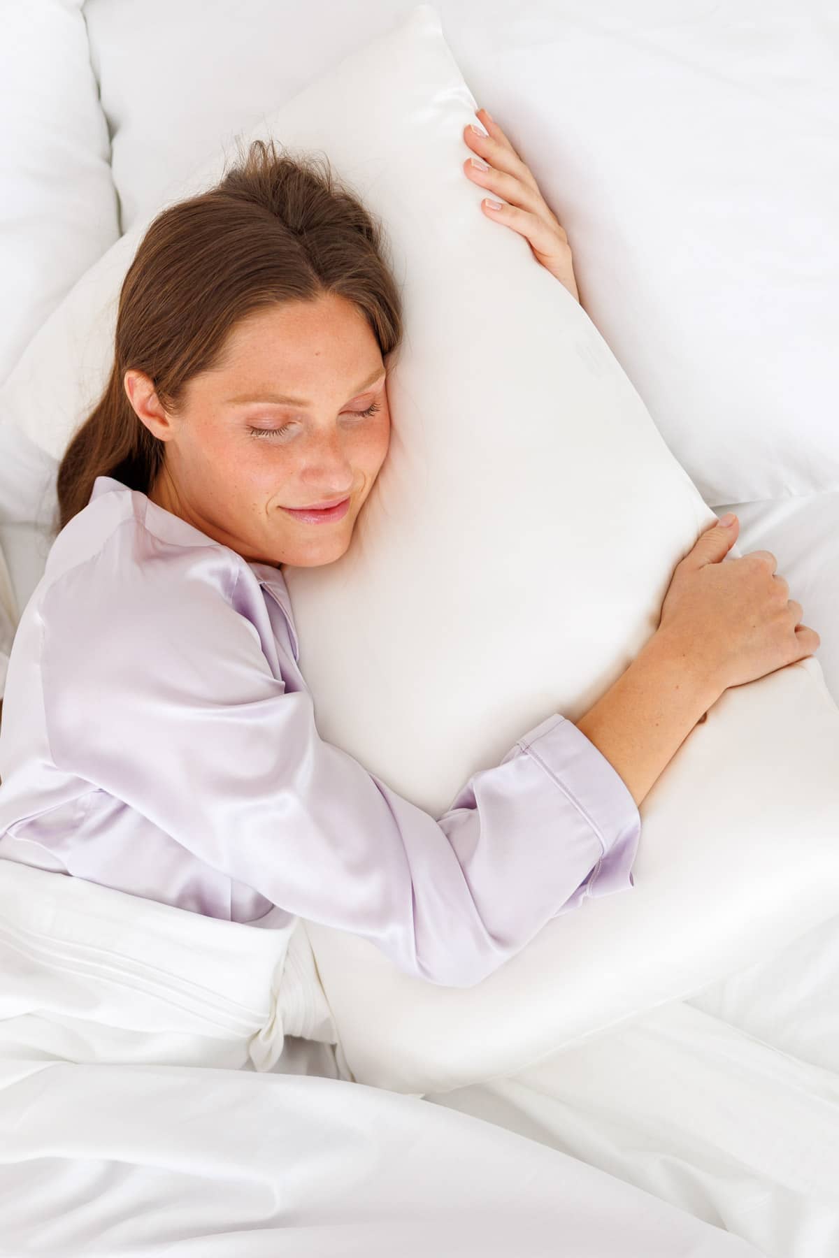 Woman sleeping peacefully on soft white silk sheets with a smooth, lustrous finish.