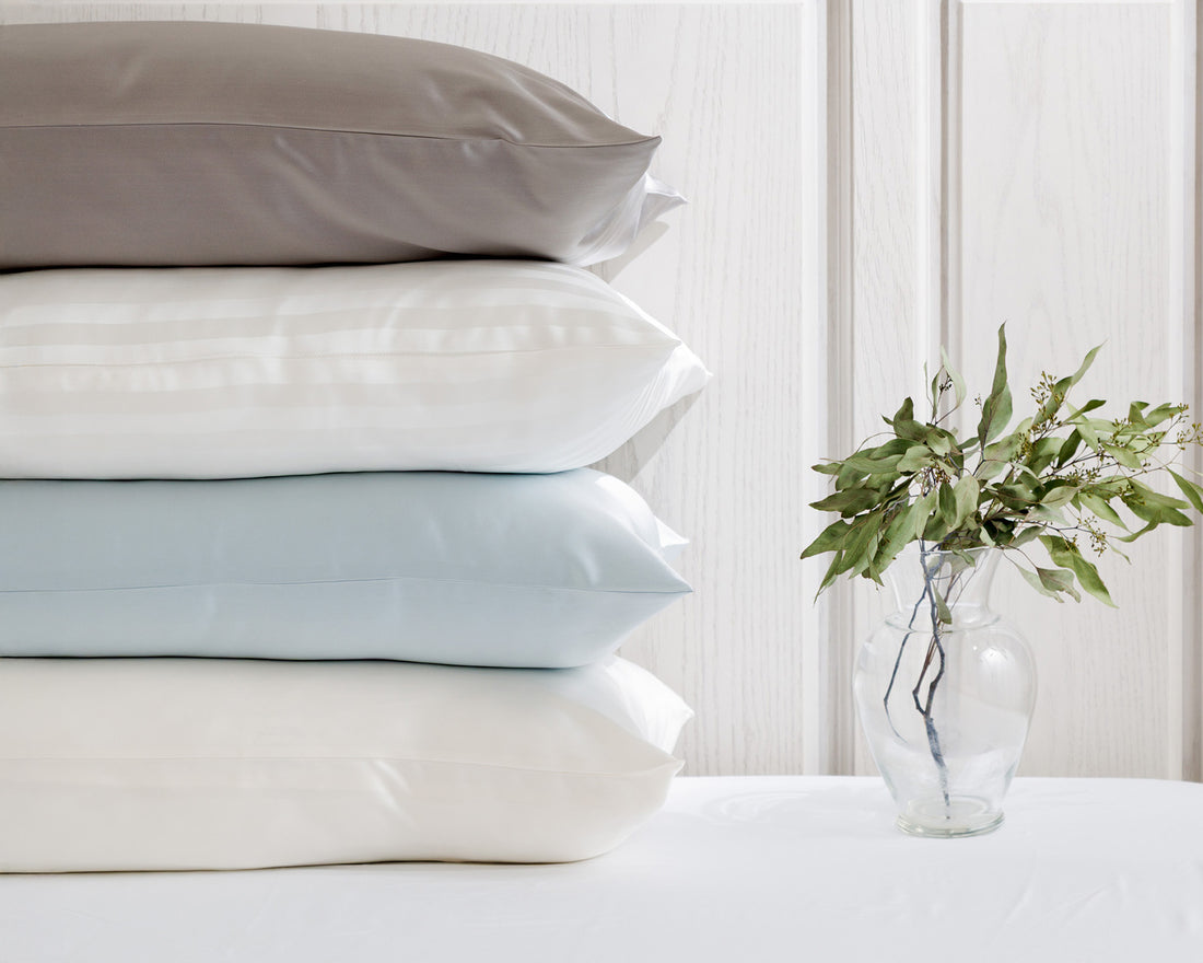 Stack of pillows in various colors on a white surface with a vase of greenery in the background.