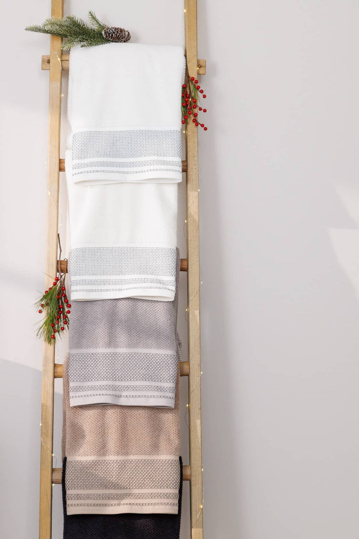 Four folded woven towels in white, light gray, taupe, and dark charcoal, hanging on a wooden ladder decorated with pine branches and red berries against a light gray wall.