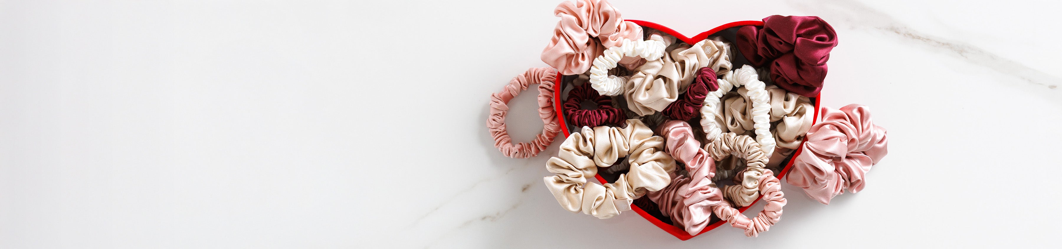 Heart-shaped container with silk scrunchies on a white background