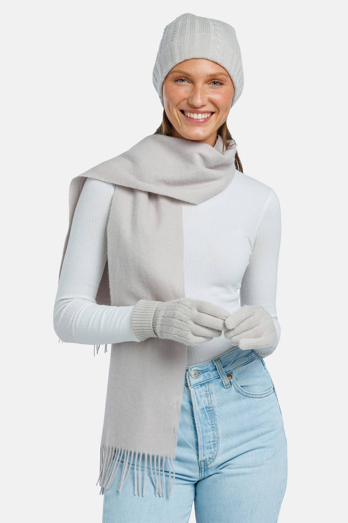 women wearing a light gray cashmere hat glove and scarf set over a white top and jeans