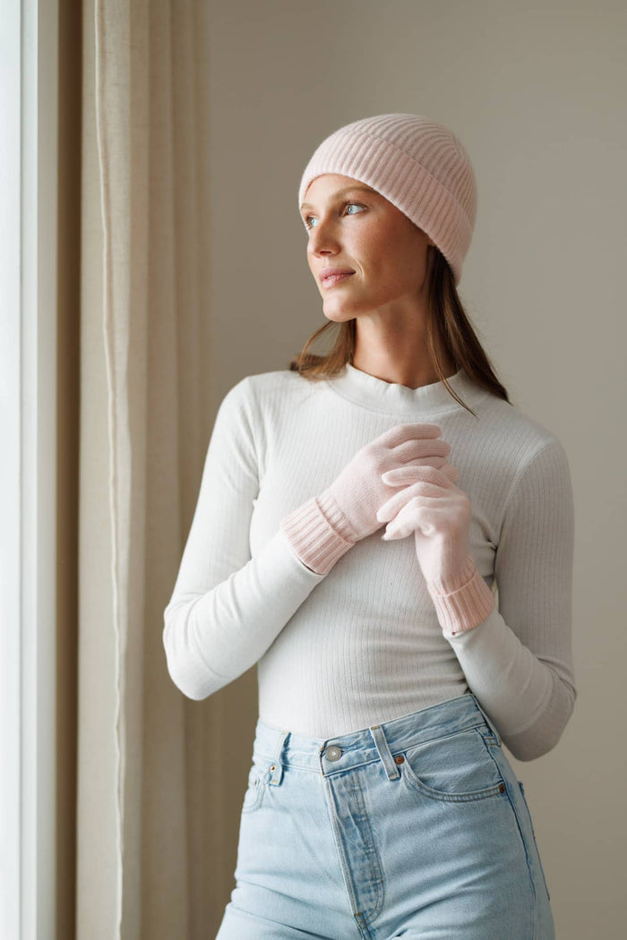 Pink cashmere knit beanie and matching gloves on model with white top.