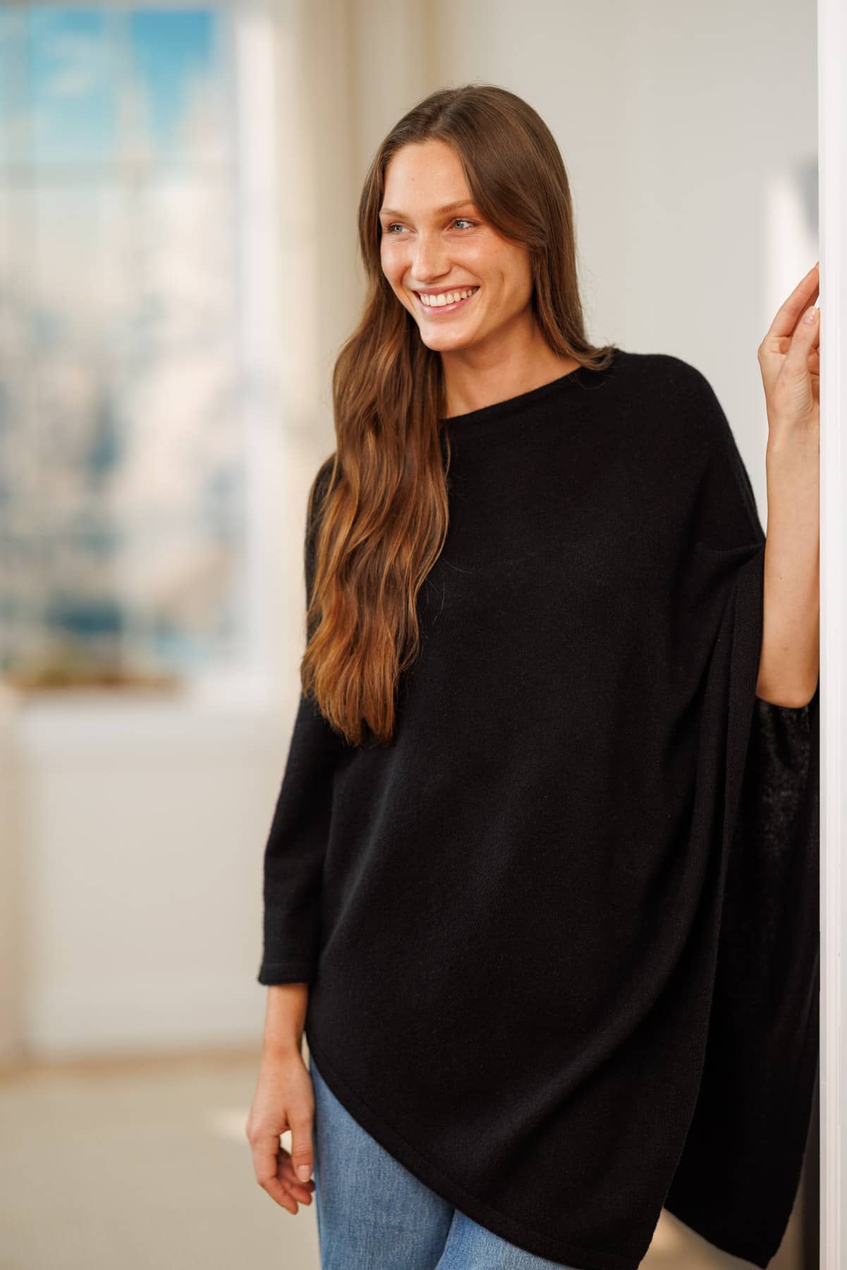 women wearing a black cashmere poncho over jeans in a living room setting.