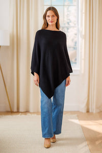 women wearing a black cashmere poncho over jeans in a living room setting.