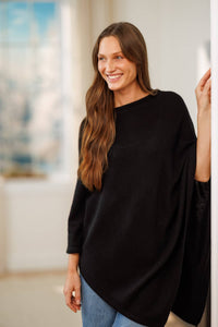 women wearing a black cashmere poncho over jeans in a living room setting.