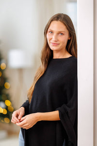 women wearing a black cashmere poncho over jeans in a living room setting.