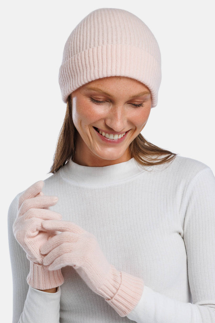 Pink cashmere knit beanie and matching gloves on model with white top.