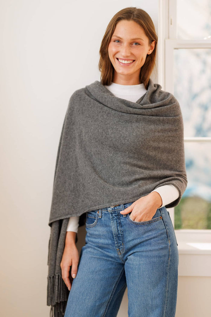 Gray cashmere shawl with fringe draped over white long-sleeve top and jeans.