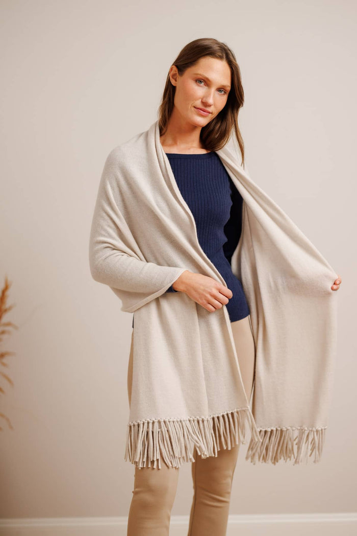 Light gray cashmere shawl with fringed edges worn over dark top and tan pants.