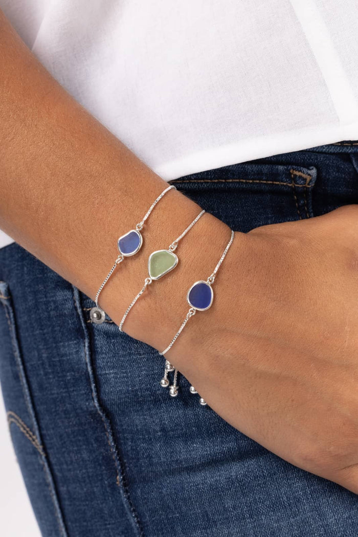Silver chain bracelets with cobalt and seafoam silk beads on wrist against white top and denim jeans.