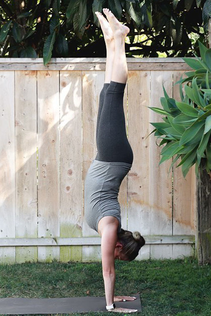 Light heather gray silk tank top paired with black leggings worn by a woman doing a handstand outdoors.